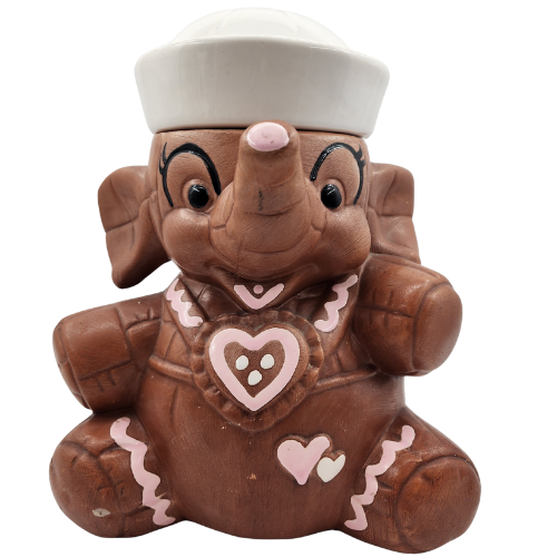 A ceramic figurine of a cartoon elephant wearing a white chef's hat and a pink heart with a white border on its chest, decorated with pink hearts and zigzag patterns.
