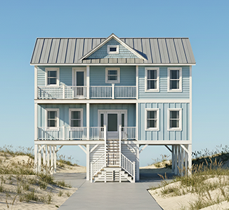 A three-story beach house painted in light blue with white trim, featuring multiple windows, balconies with white railings, a metal roof, stairs leading to the only front door, and sand dunes with grass underneath.