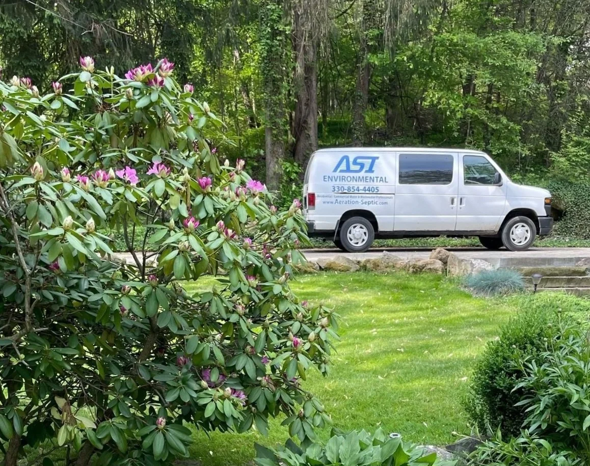 ASI residential division service van parked in a driveway surrounded by green bushes and pink flowers and trees