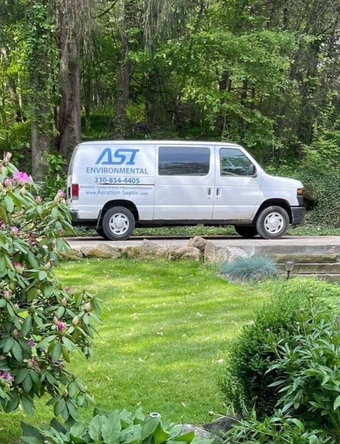 A white van labeled 'ASI Environmental' parked on a driveway in a green residential yard, with trees and shrubs surrounding the area.