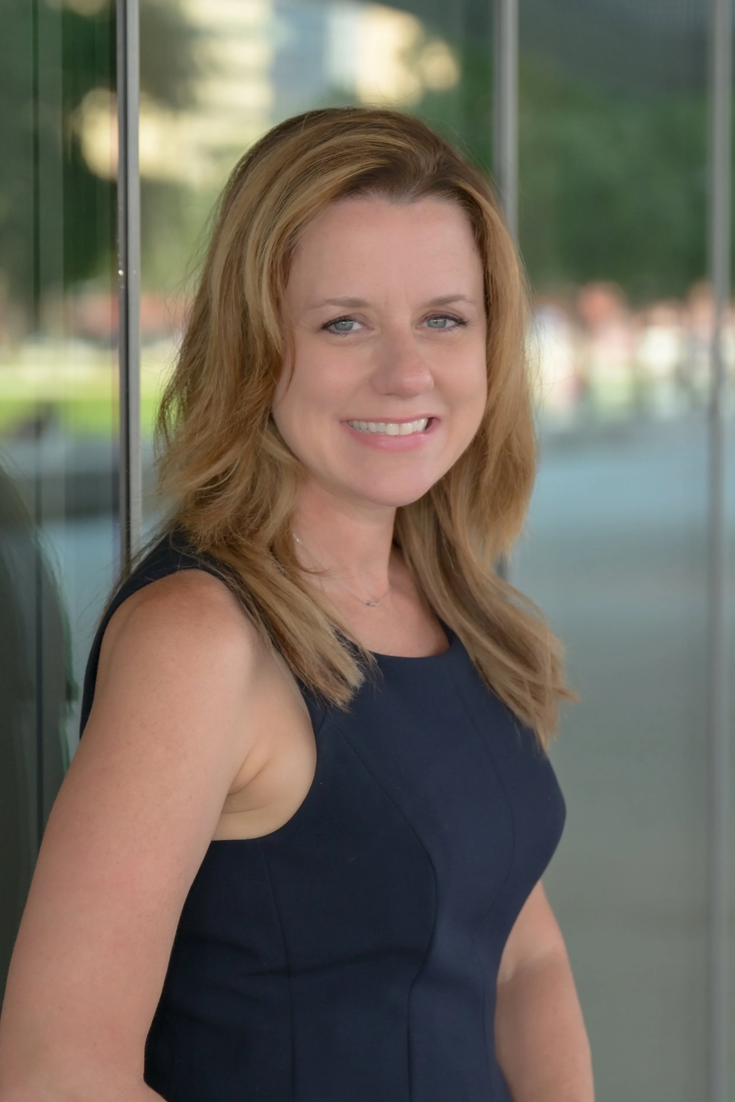 This photo shows Dr. Rebekah Hellier smiling in a navy blue dress outside of her office in downtown Tampa, Florida.