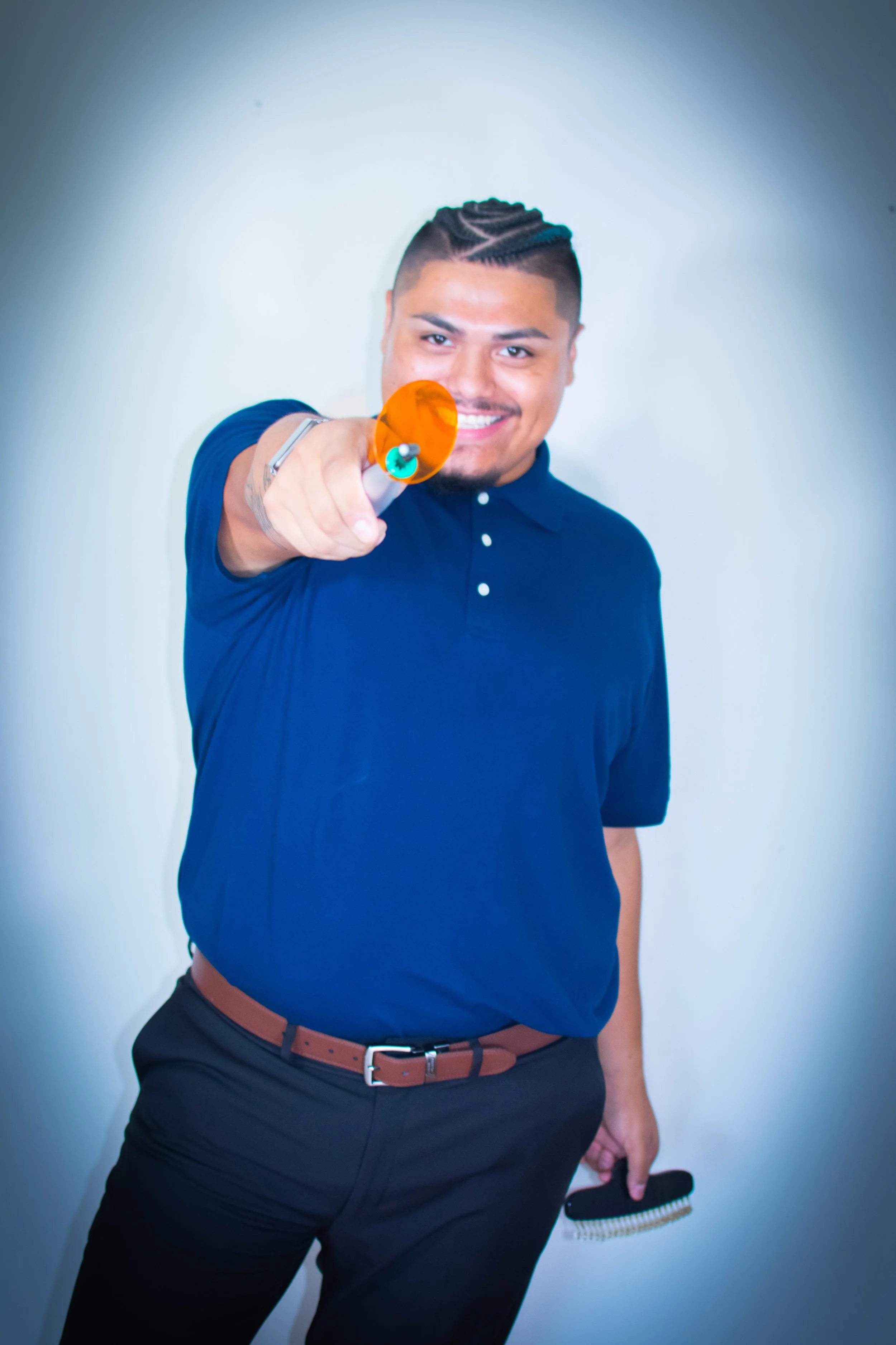 A smiling man with short, styled hair pointing a paint roller towards the camera.