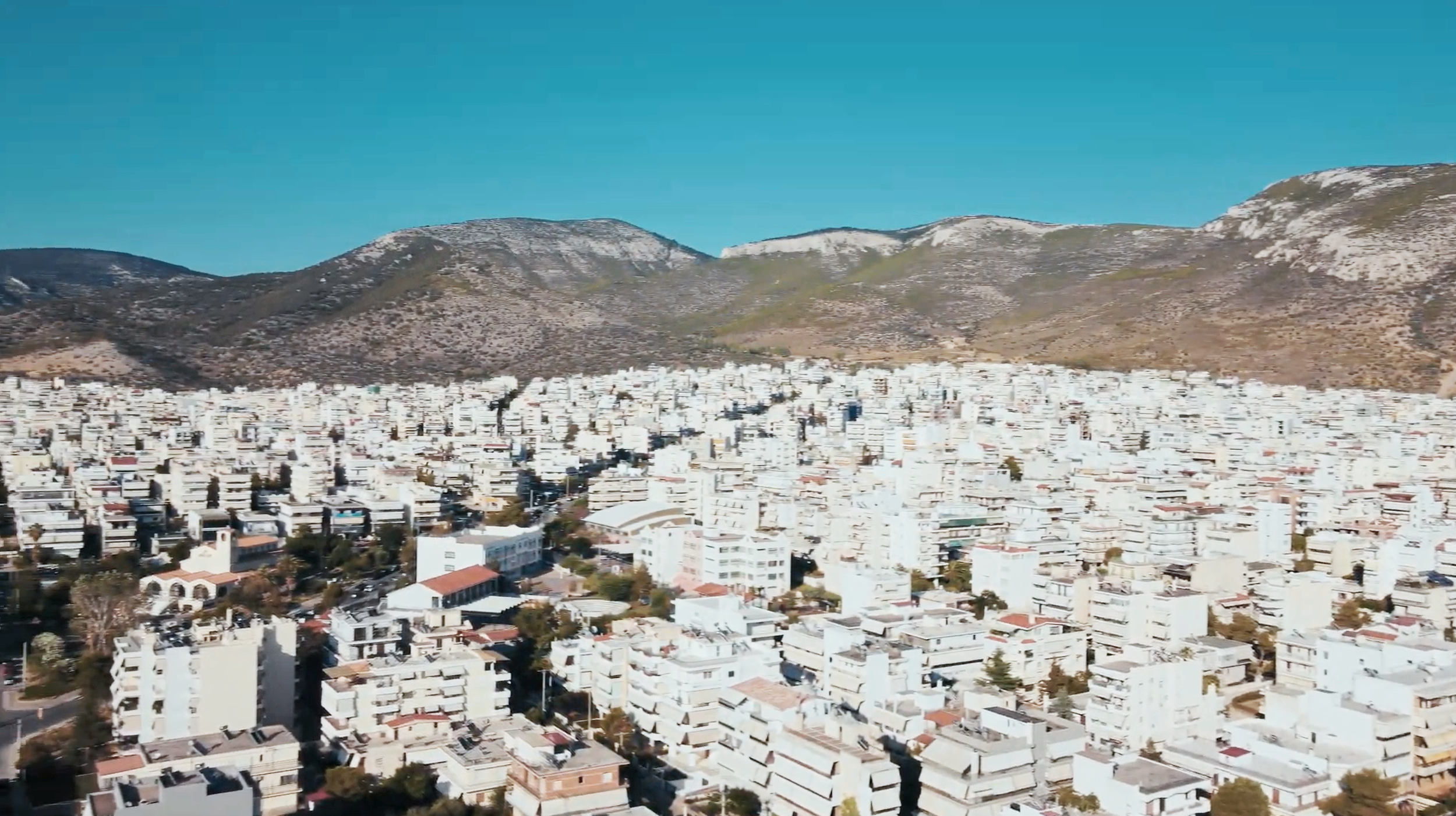 Aerial view of a densely populated city with many white buildings, surrounded by mountains under a clear blue sky.