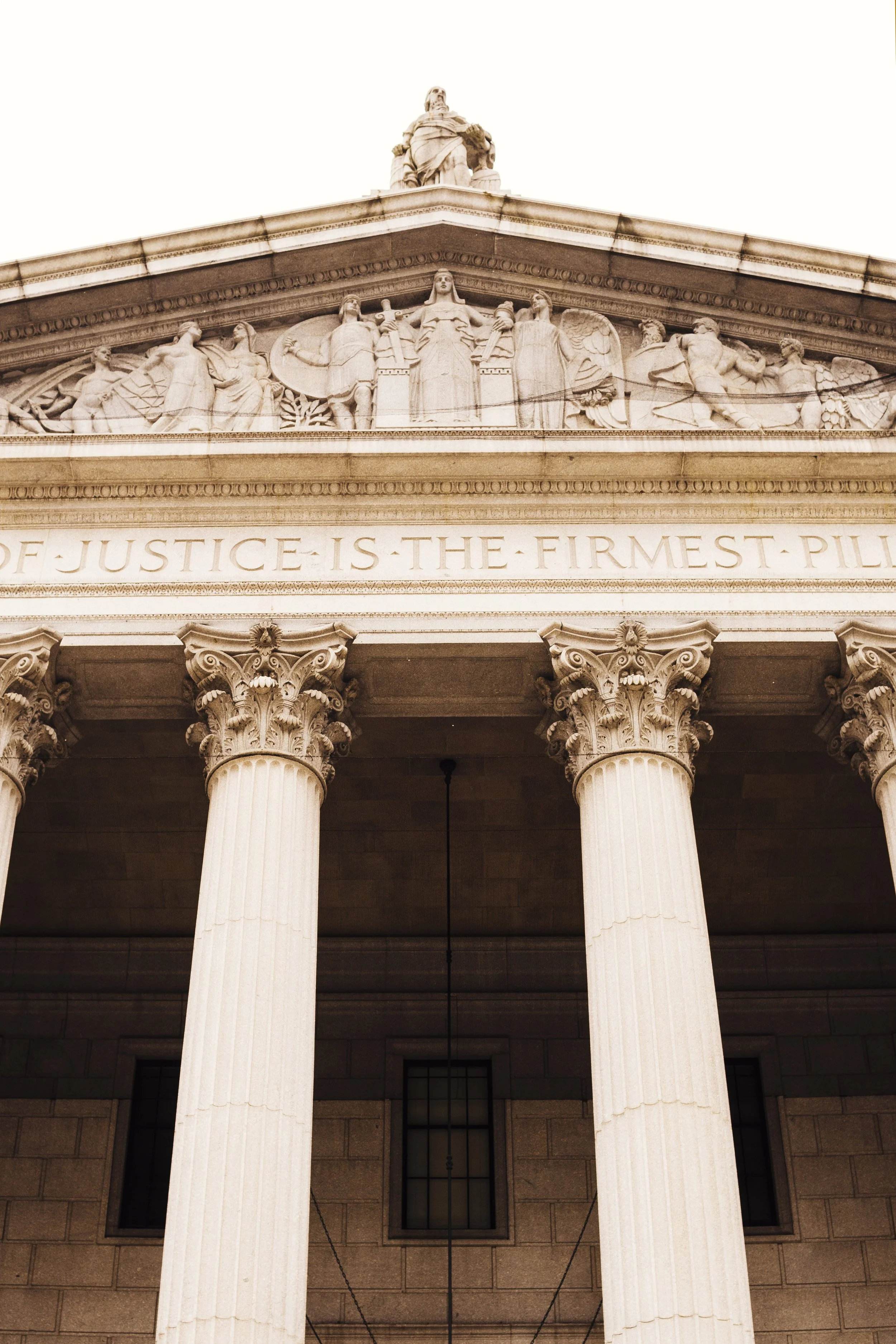 Close-up of the front facade of a classical government building with large columns, a detailed pediment sculpture, and an inscription about justice.