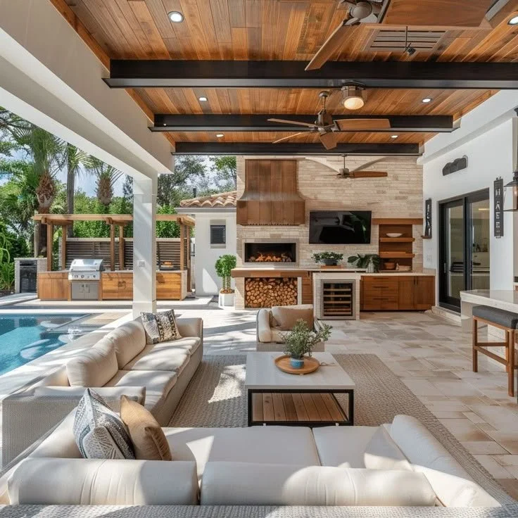A modern outdoor living space featuring a pool, comfortable seating, a fireplace, a mounted TV, a wood-paneled ceiling with ceiling fans, and a built-in barbecue with a wood storage area.