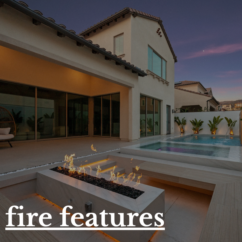 Modern backyard with a rectangular fire feature, swimming pool, and patio seating at dusk, with a two-story house in the background.