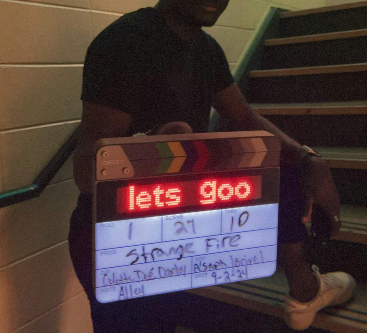 Person sitting on stairs holding a clapperboard with a message that says "let's go."