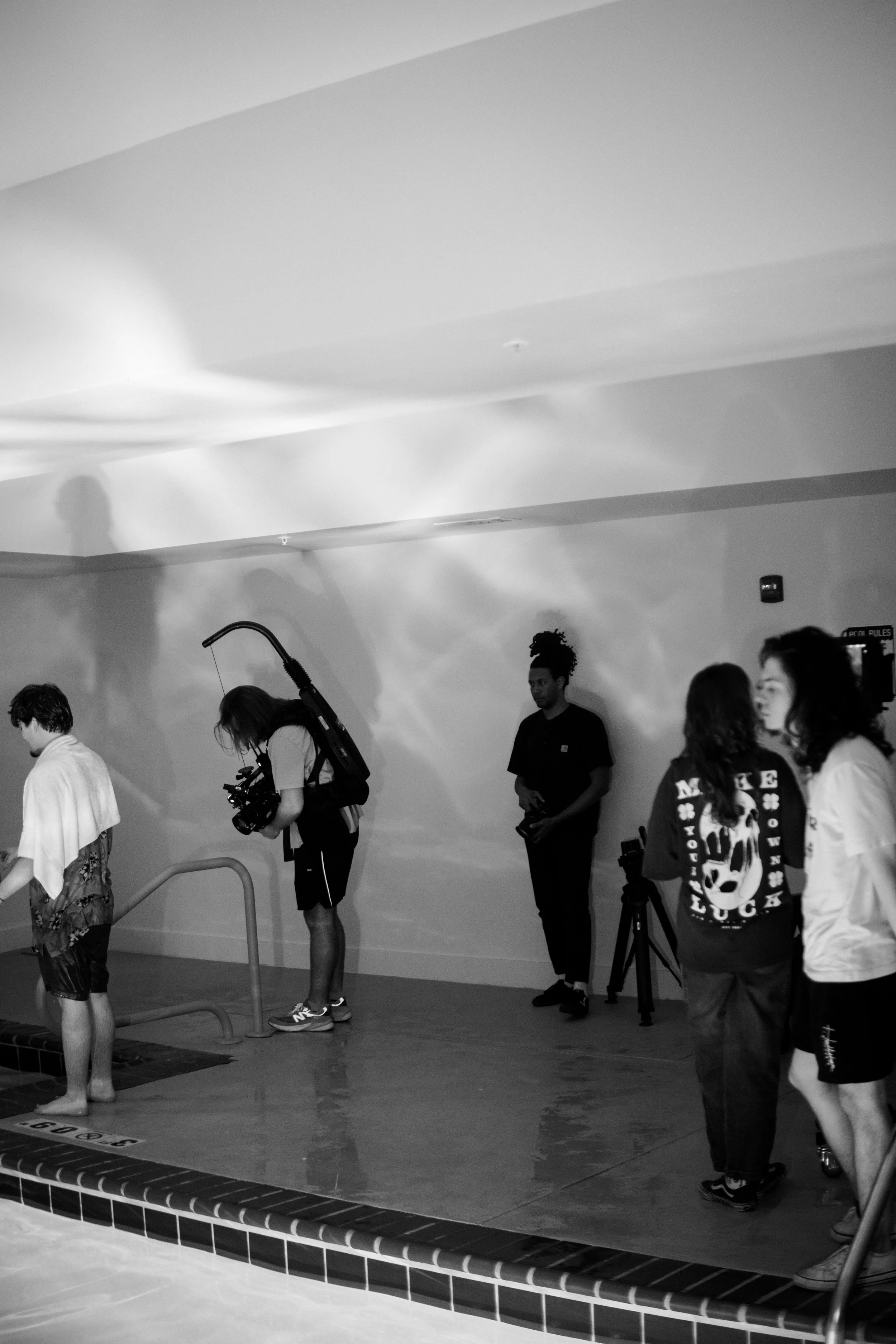 People at the indoor pool, with some filming and others standing near the wall, black and white photo.