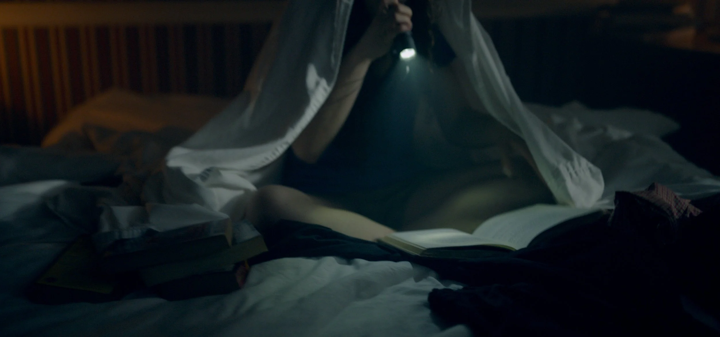 Person in bed using a flashlight to read a book in a dark room
