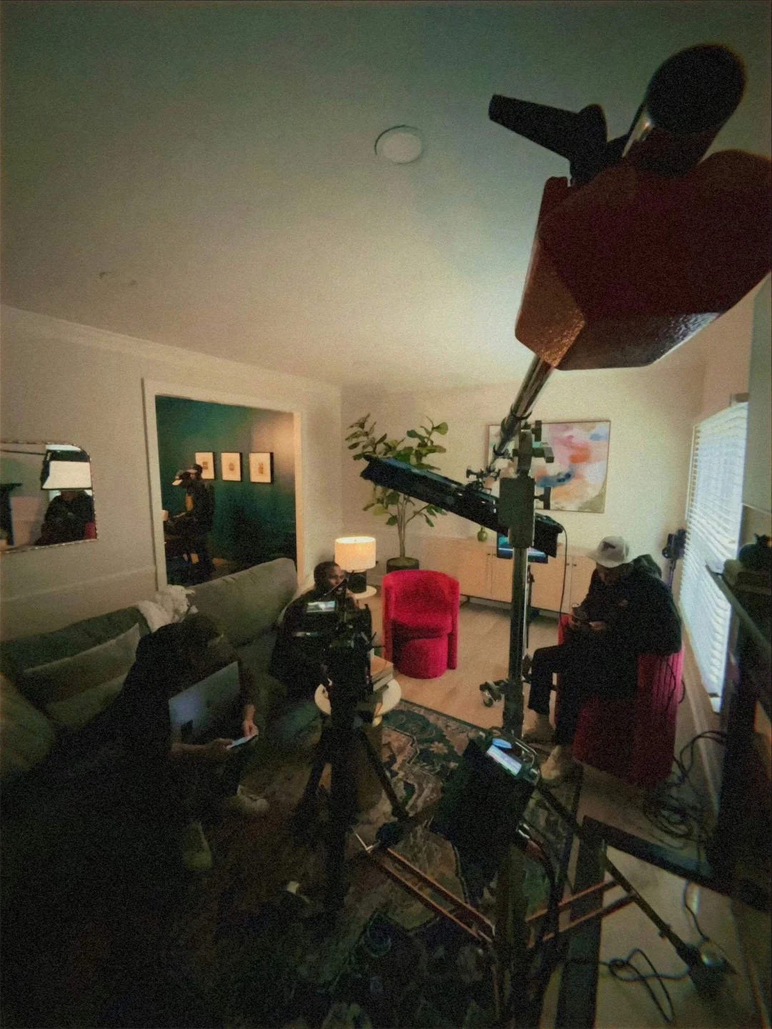 Indoor scene with multiple people, filming equipment, and furniture, indicating a filming or interview setup.