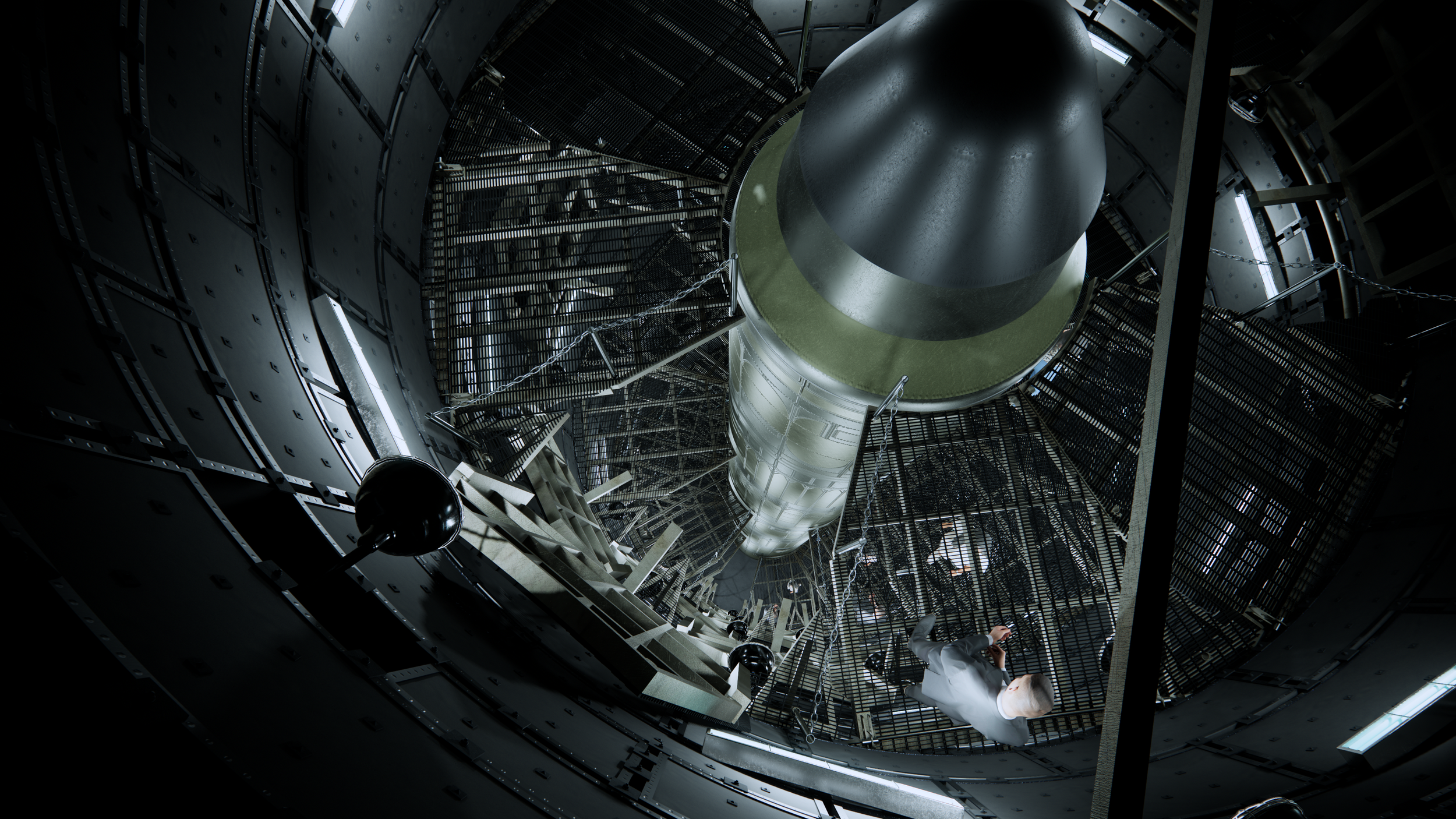 A person taking a photo inside a large, cylindrical rocket silo with a rocket in the center, surrounded by metal walkways and mesh cages.