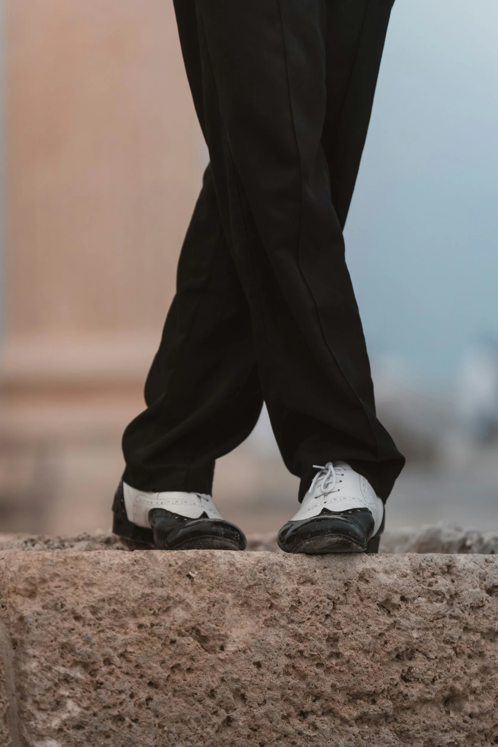 Close-up of a person wearing black pants and black and white shoes, standing on a stone surface.