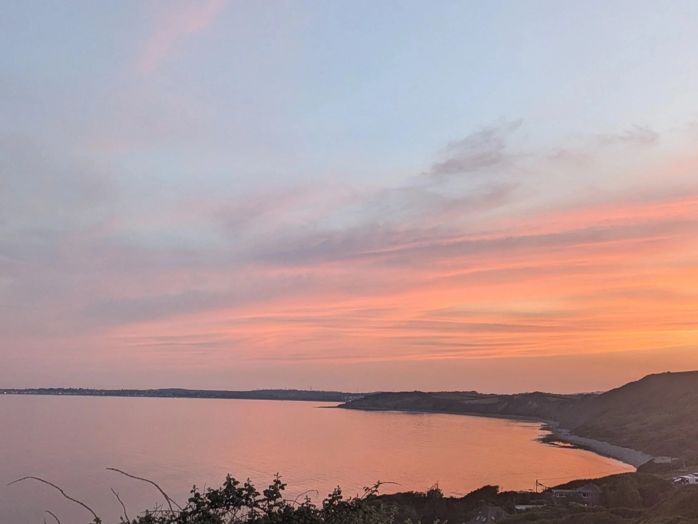 Sunset over coastline with colorful sky and distant hills.
