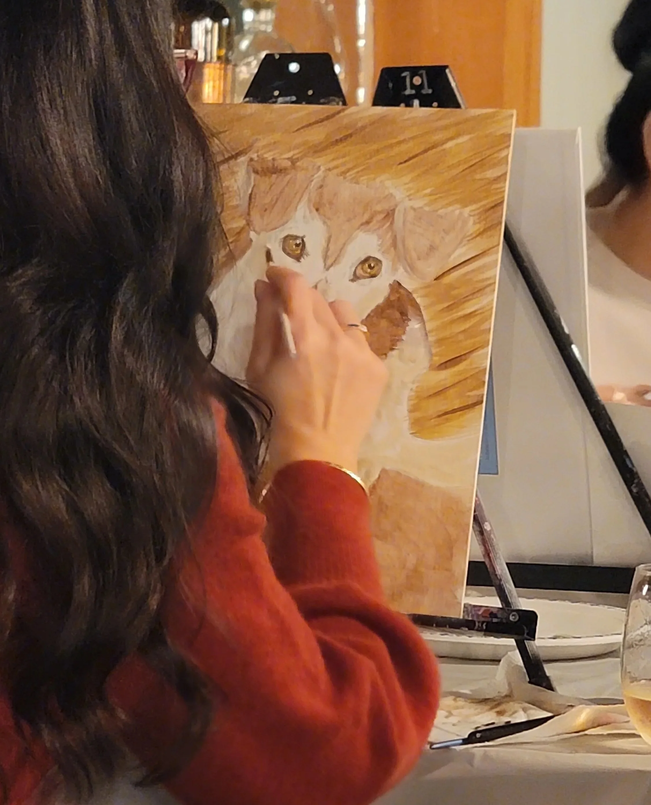 A woman painting a detailed portrait of a dog on a canvas, with bottles and glasses visible in the background.  Art Classes, Workshops and Parties with Party with Laura. Available in Cloverdale, Bc Surrey, Langley, White Rock, Richmond, Vancouver, an