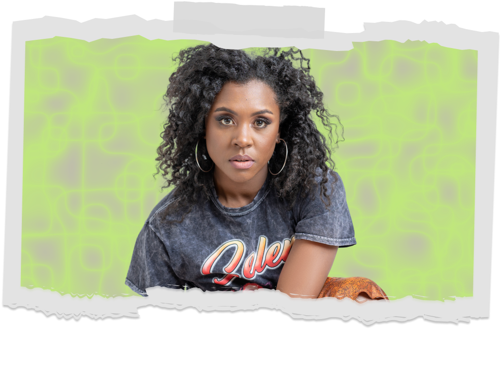 A young woman with curly black hair, wearing large hoop earrings, and a vintage-style black t-shirt, sitting against a green background with neon-like patterns.