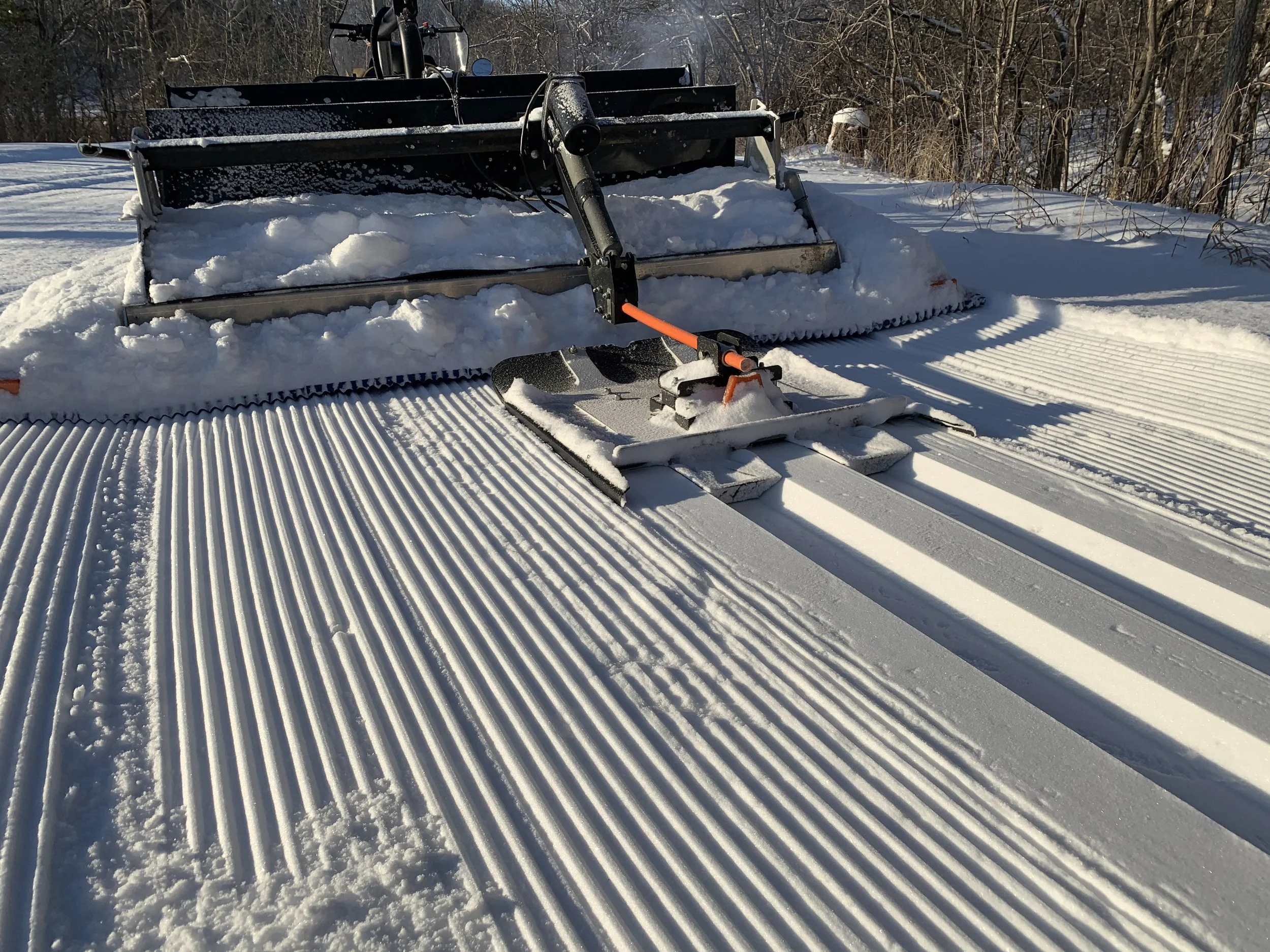 A snow grooming machine on a snowy landscape, creating corduroy patterns in the snow for snowboarding or skiing.
