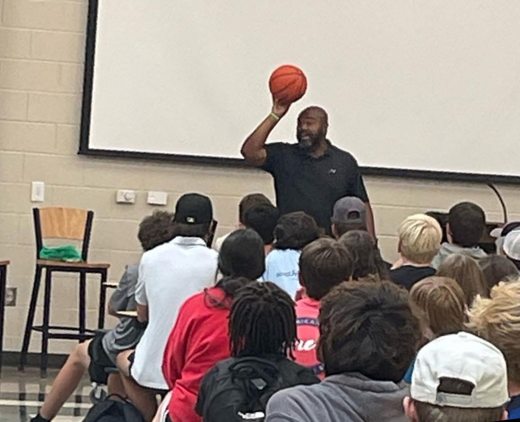 A man holding a basketball in a classroom with students attentively listening.
