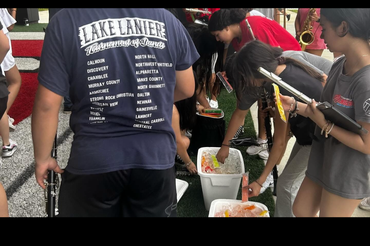 Group of people gathered around a container of ice and candy, with some holding clipboards, at an outdoor event.