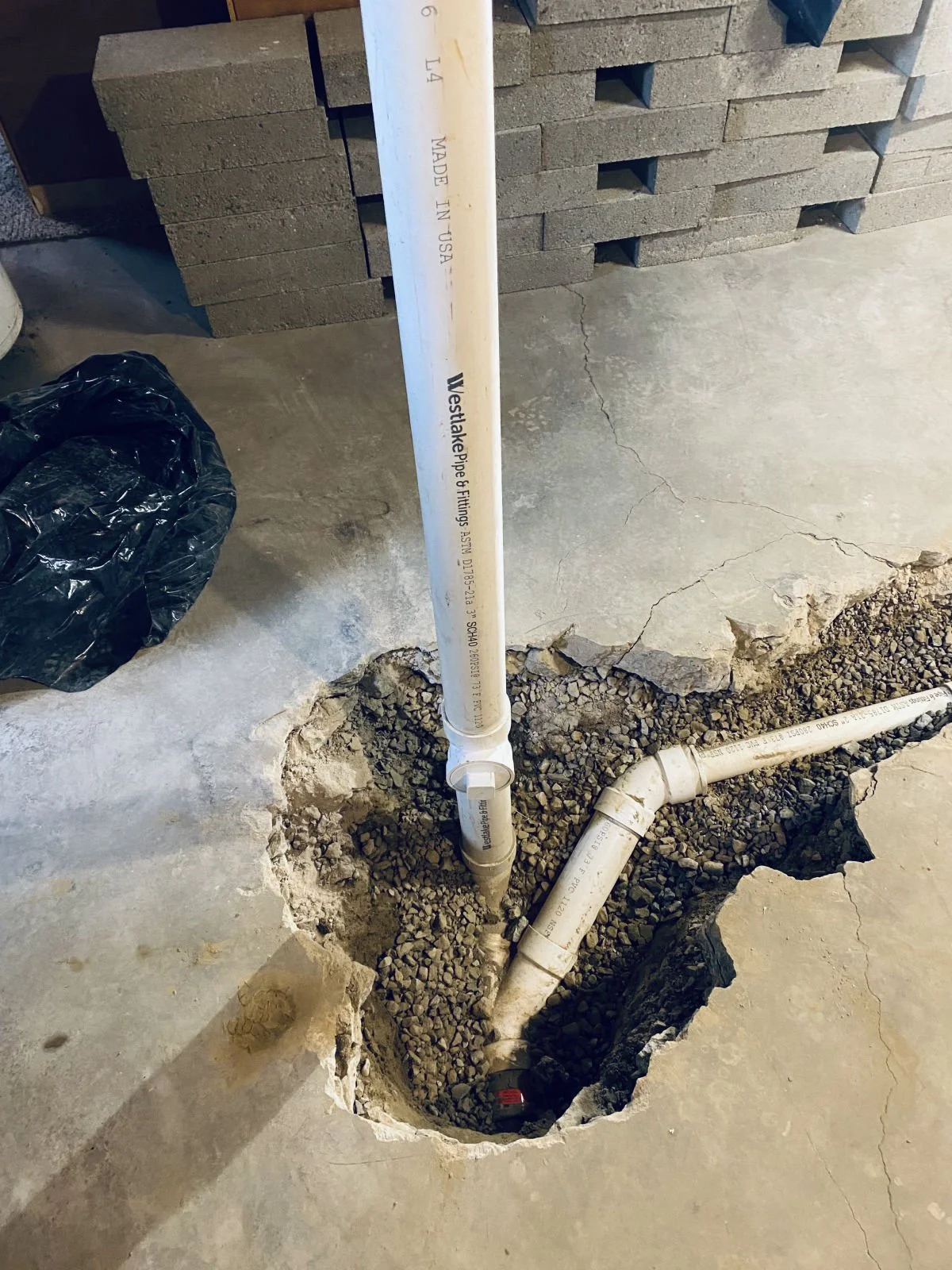 New PVC drain stack tied into the line below a basement floor, set in gravel
