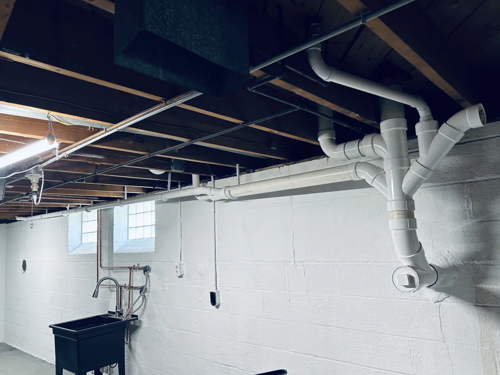 New PVC drain piping with wyes and cleanouts running along a basement wall