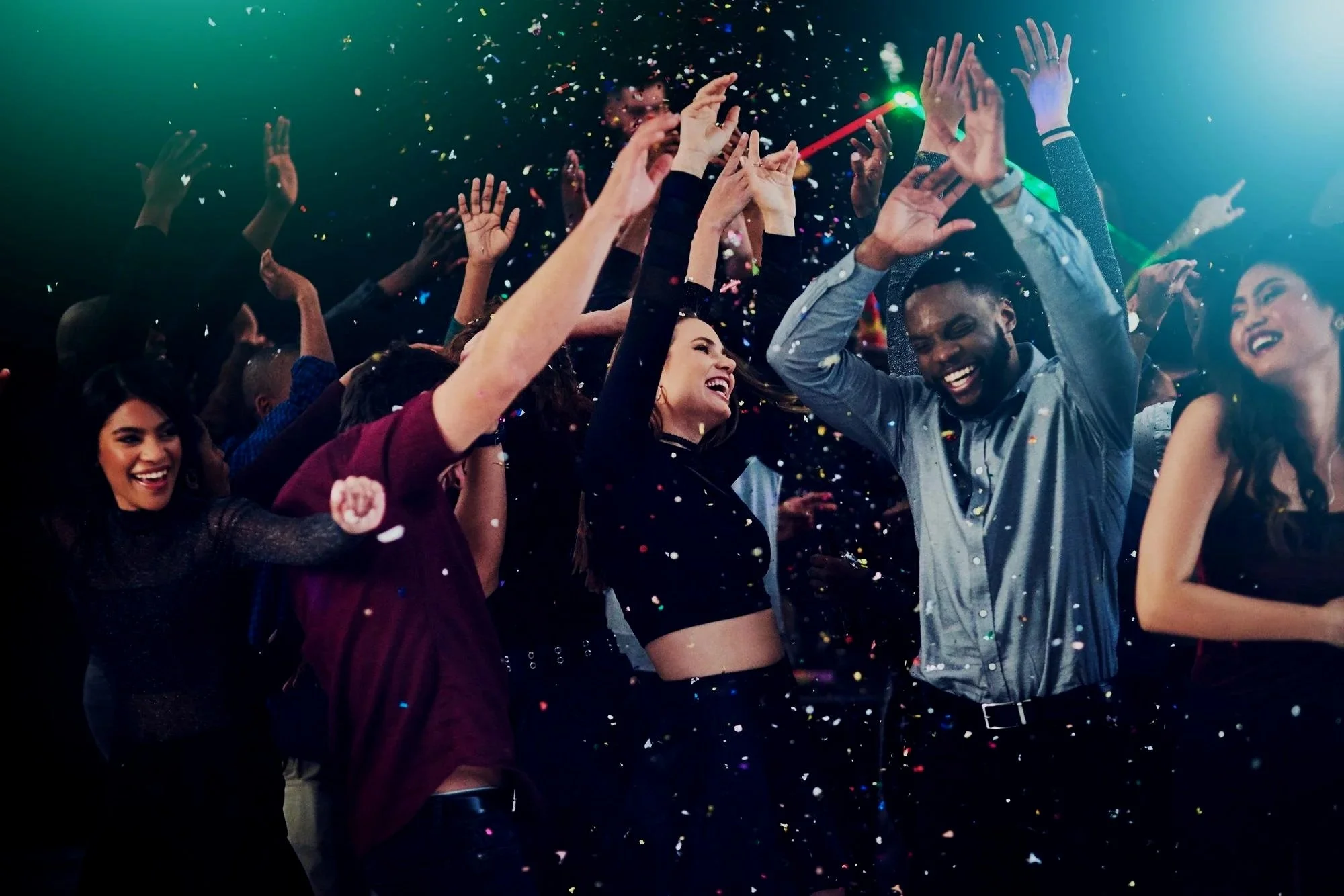 People dancing at a party with colorful confetti and green and blue lights.