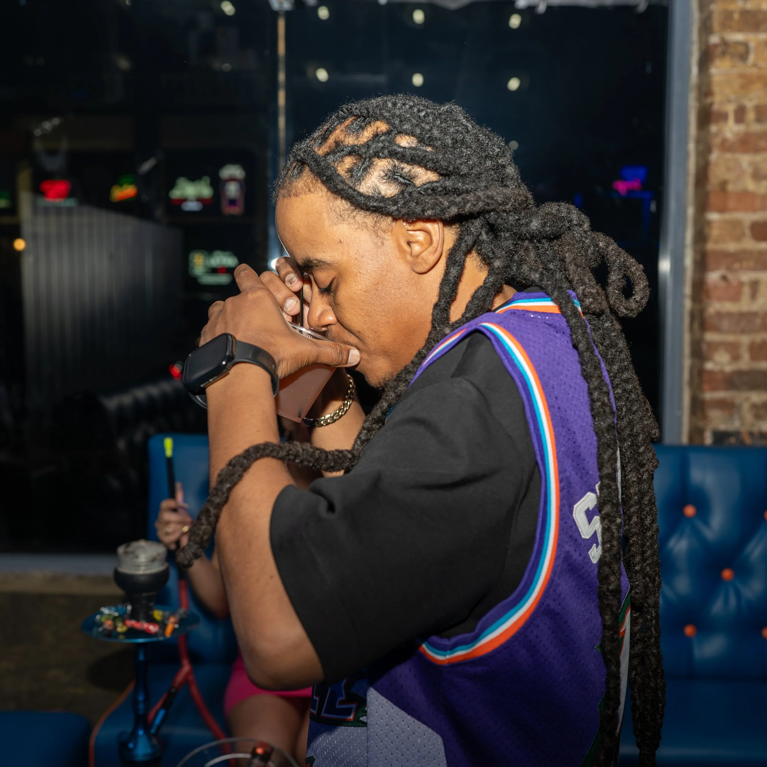 A person with dreadlocks is praying or meditating with hands clasped and eyes closed, wearing a colorful basketball uniform with rainbow stripes on the sleeves.