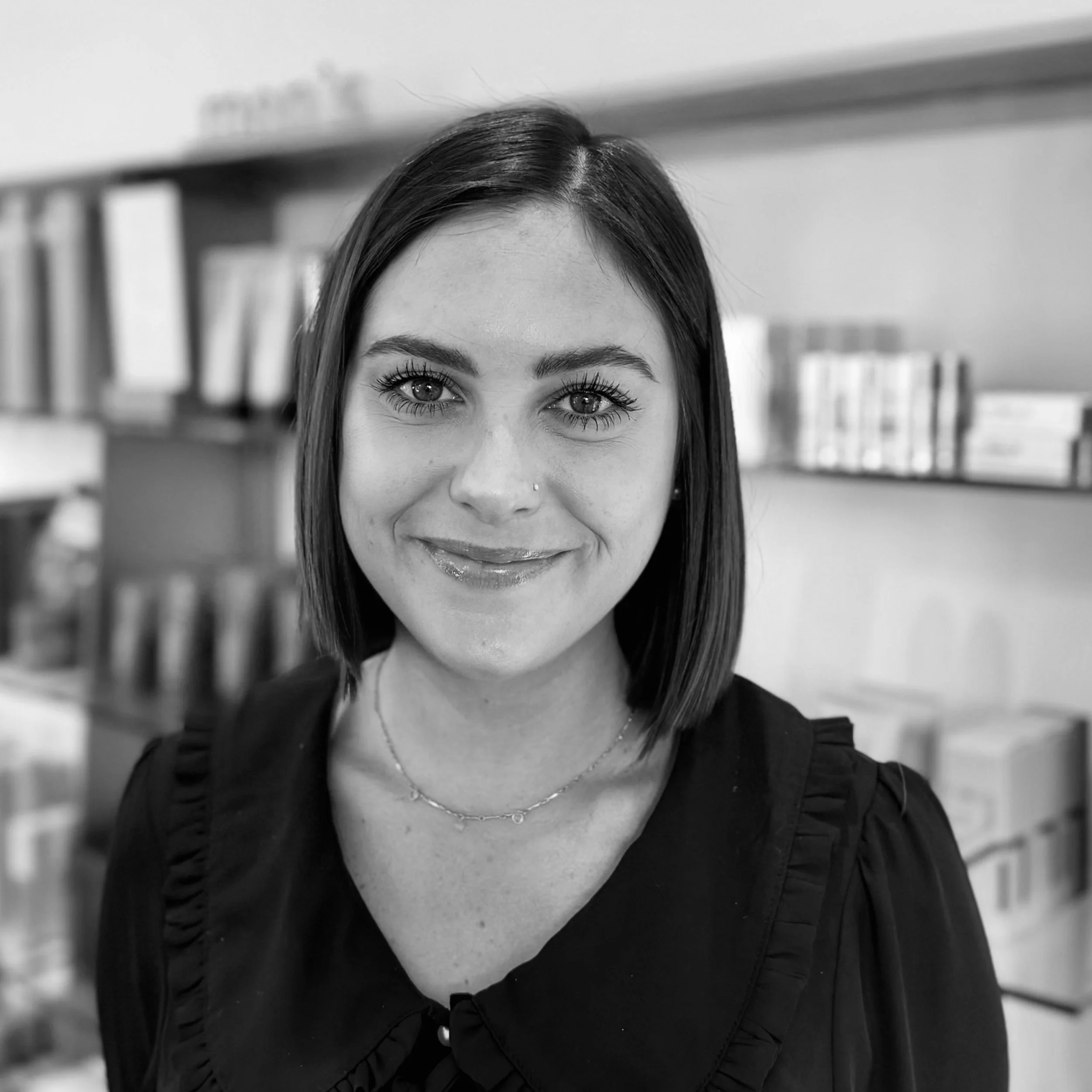 Black and white portrait of a smiling woman with wavy shoulder-length hair, wearing a blazer and a necklace with a heart pendant.