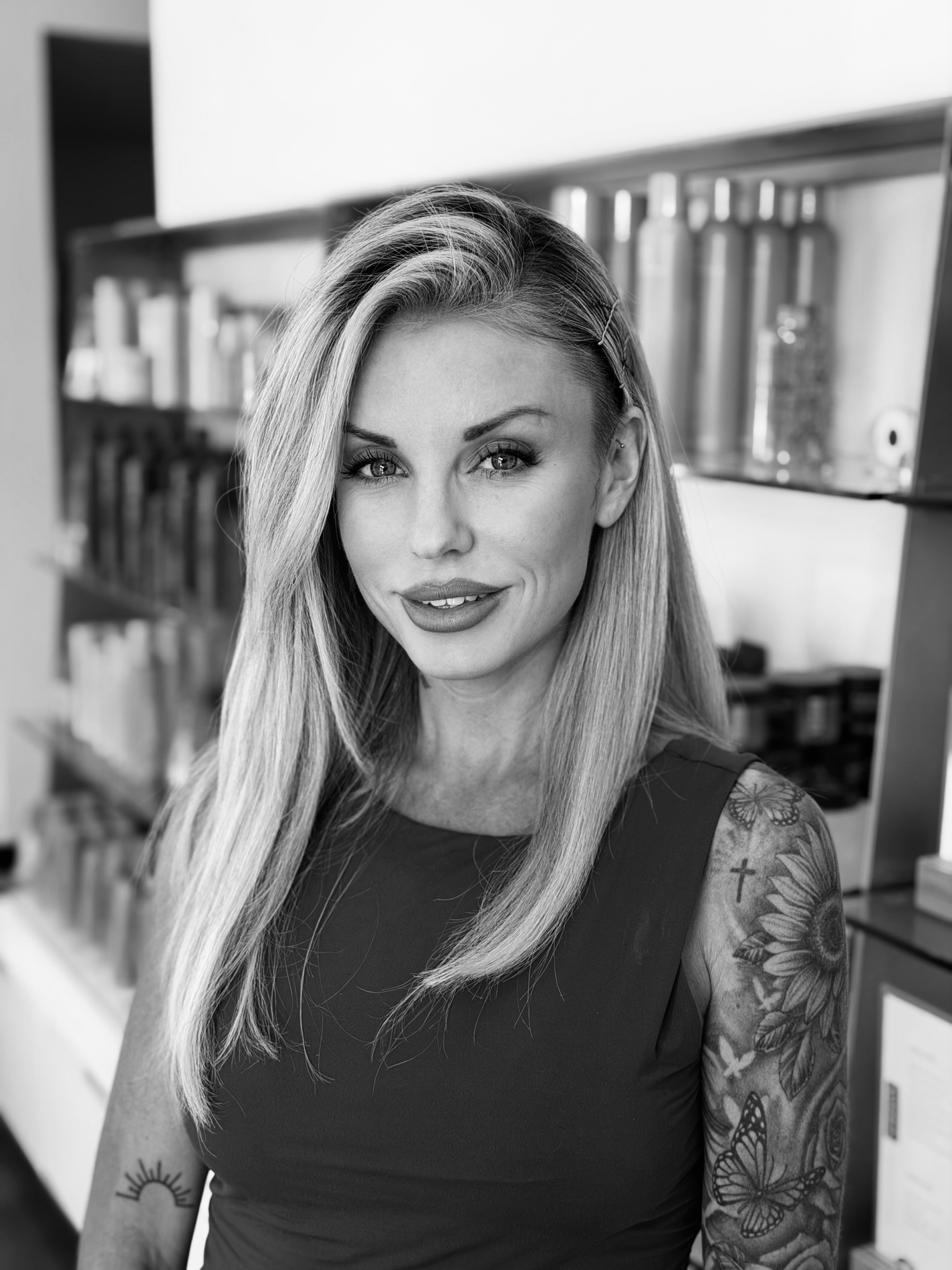 A black-and-white photo of a woman with long blonde hair, wearing a headband and a lace top, smiling at the camera.