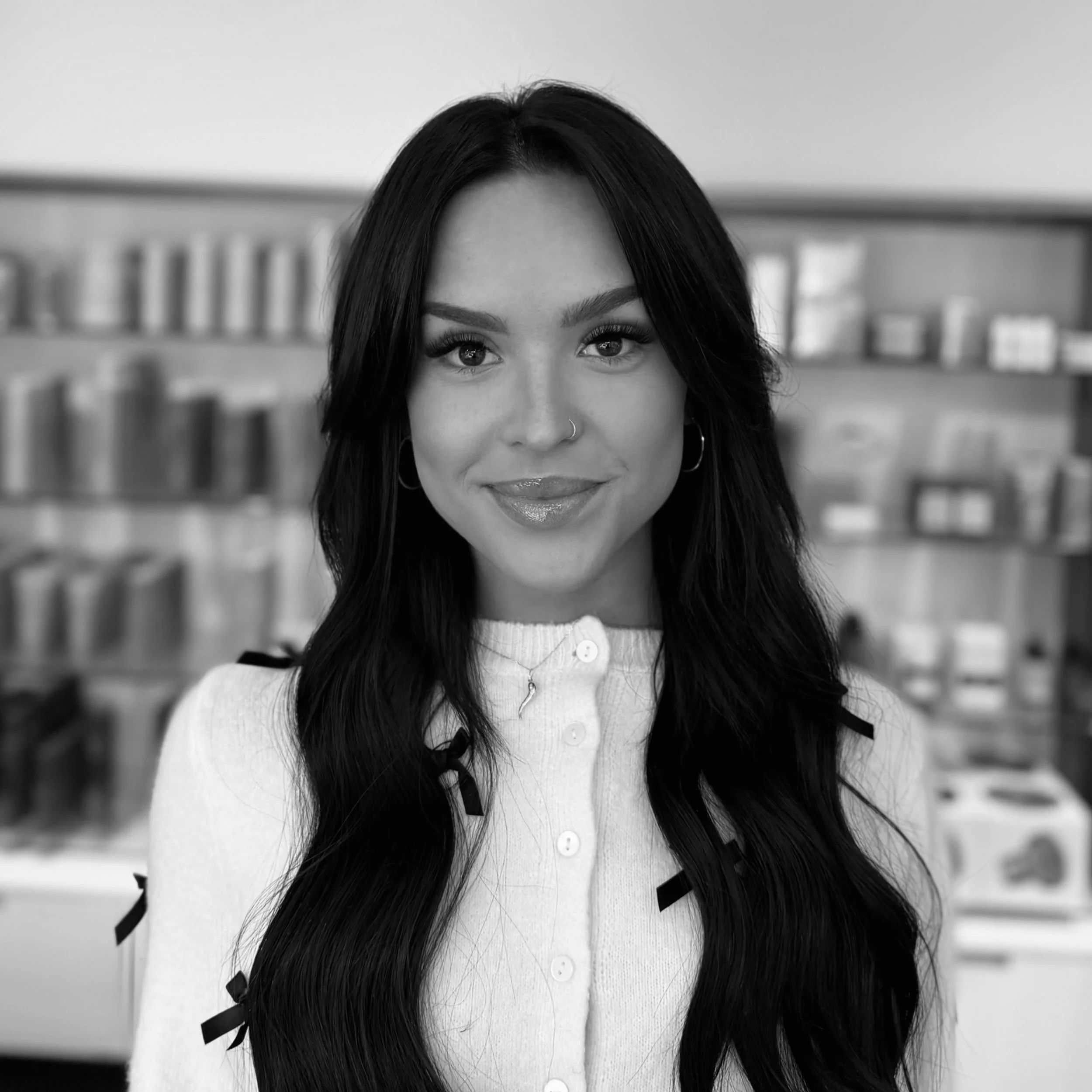 Black and white portrait of a woman with long dark hair, hoop earrings, a nose ring, and a friendly expression, against a plain light background.