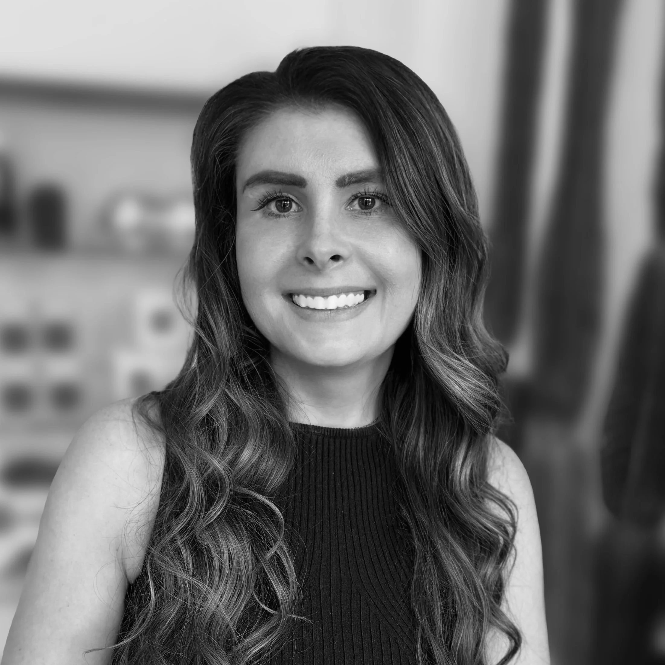Black and white portrait of a woman with wavy hair, smiling, wearing a sleeveless top.