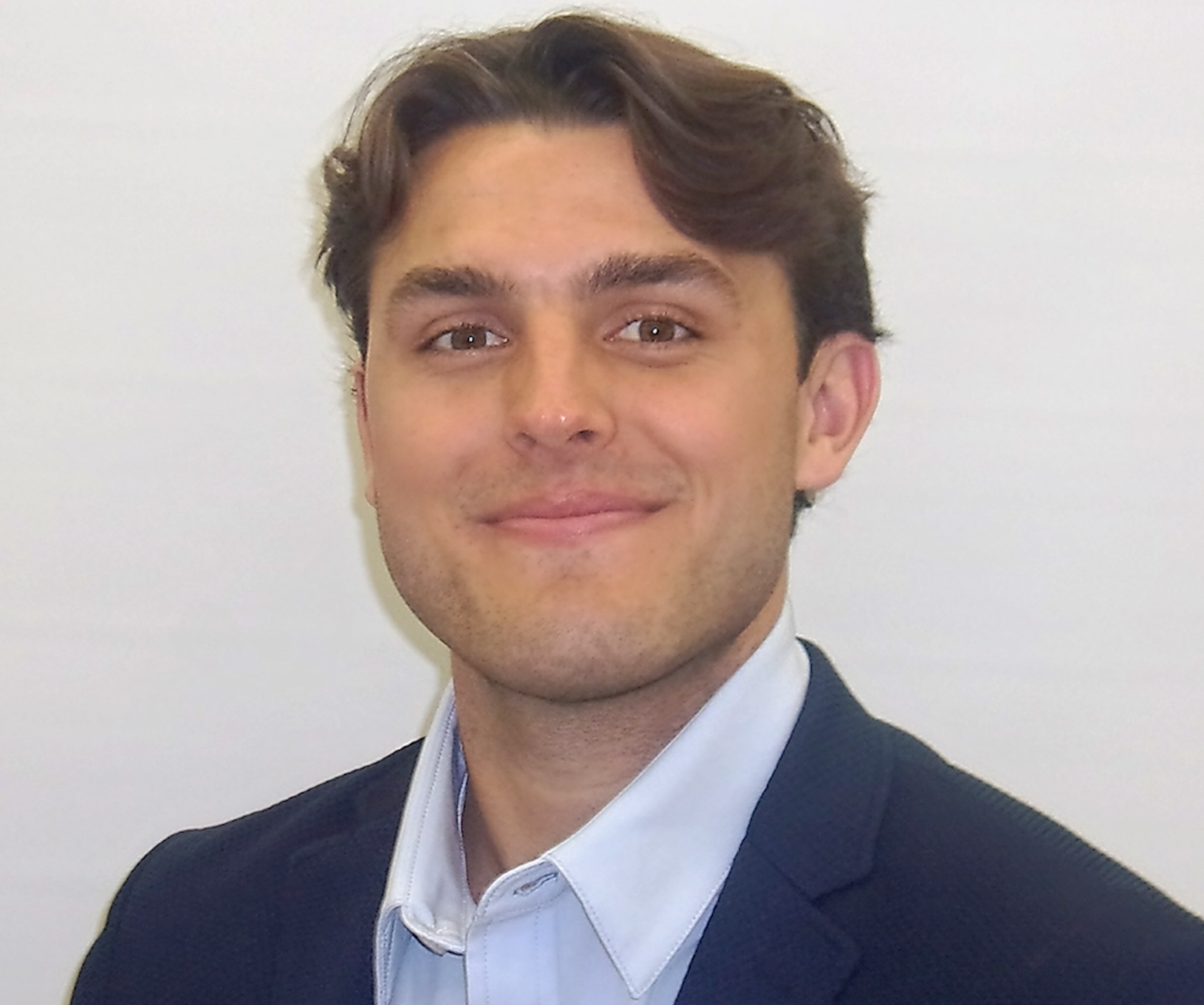 Portrait of a man with light brown hair beard in a navy blazer and light shirt against white background.
