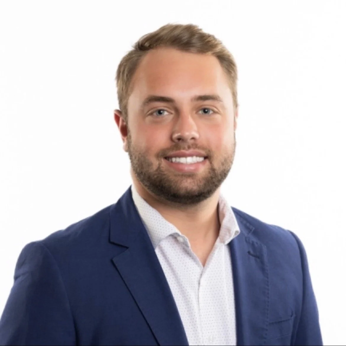 Portrait of a man with light brown hair beard in a navy blazer and light shirt against white background.