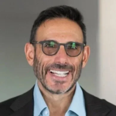 Portrait of a man in a dark suit and striped tie with arms crossed, standing against a plain background.