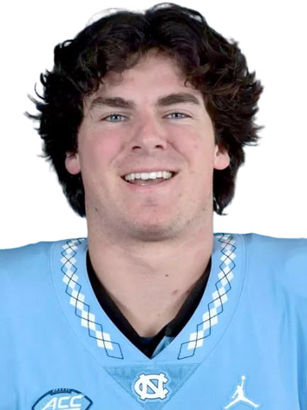 A young man with curly brown hair smiling, wearing a light blue sports jersey with the North Carolina Tar Heels logo and Nike branding.