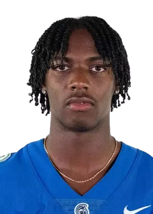 A young man with medium dark skin and dreadlocks, wearing a blue sports jersey with a Nike logo, looking directly at the camera.