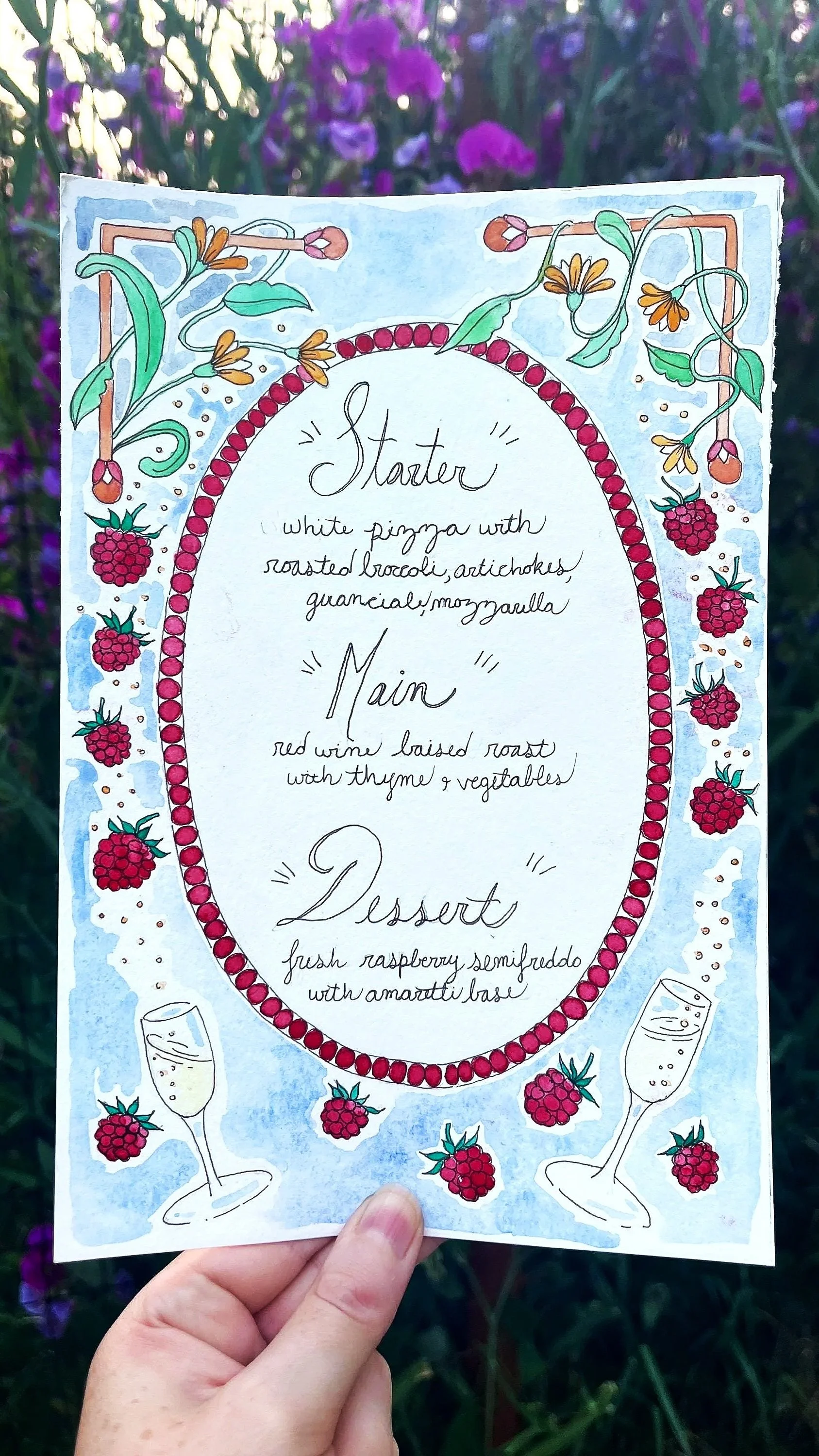 A hand holding a colorful illustrated menu with floral and berry decorations against a background of purple flowers. The menu lists starter, main, and dessert options.