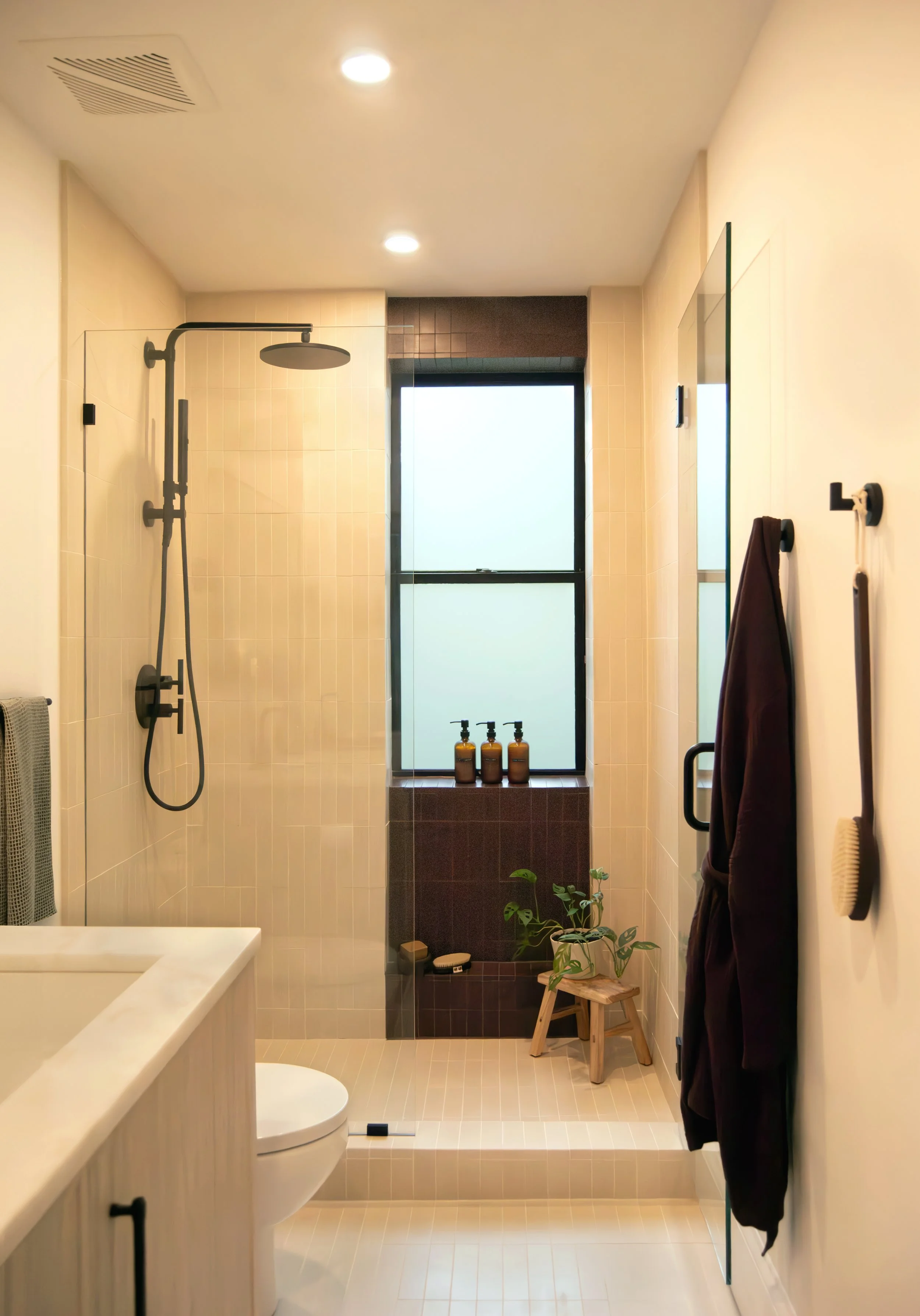 Custom glass shower with matte black fixtures, bone-colored cement floor and wall tile, and a recessed window in dark umber cement tile