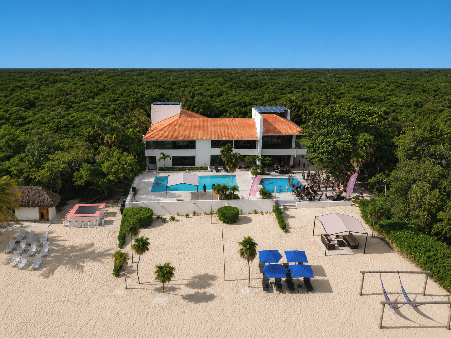 Aerial view of a modern house with a courtyard pool, surrounded by lush greenery and beach area with lounge chairs, umbrellas, and swings.