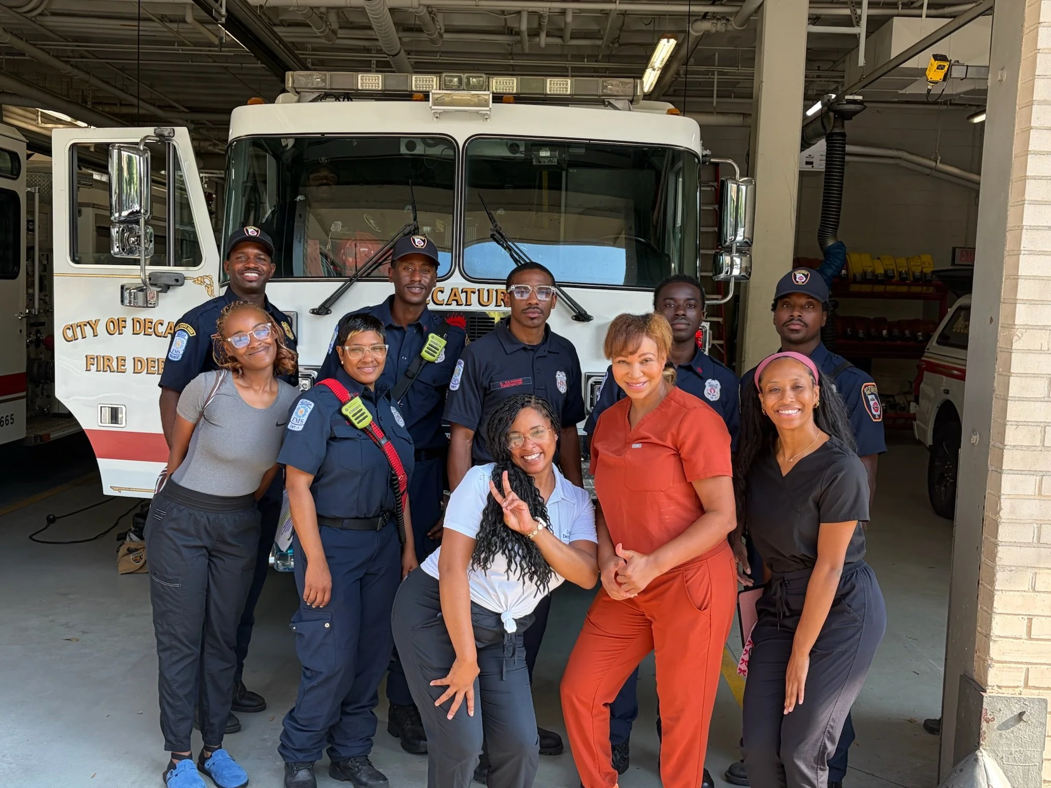 Members of Decatur Fire Rescue and the Decatur Dermatology & Aesthetics team pose together in front of a fire engine inside the Decatur fire station.