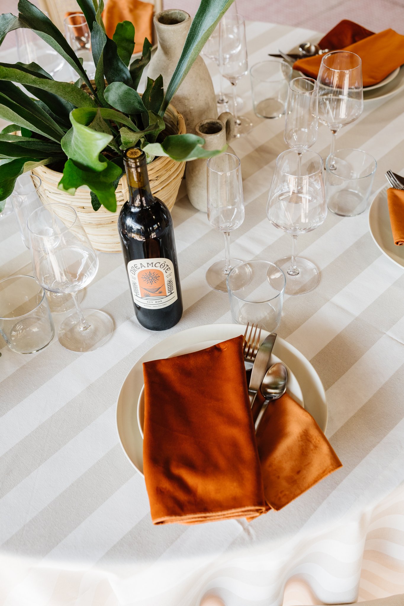 A simple upgrade can completely transform the table. Shown here, a rich orange napkin and striped linen add depth and warmth, allowing our clean slate plates and silverware to become a canvas for color, texture, and personal style.
