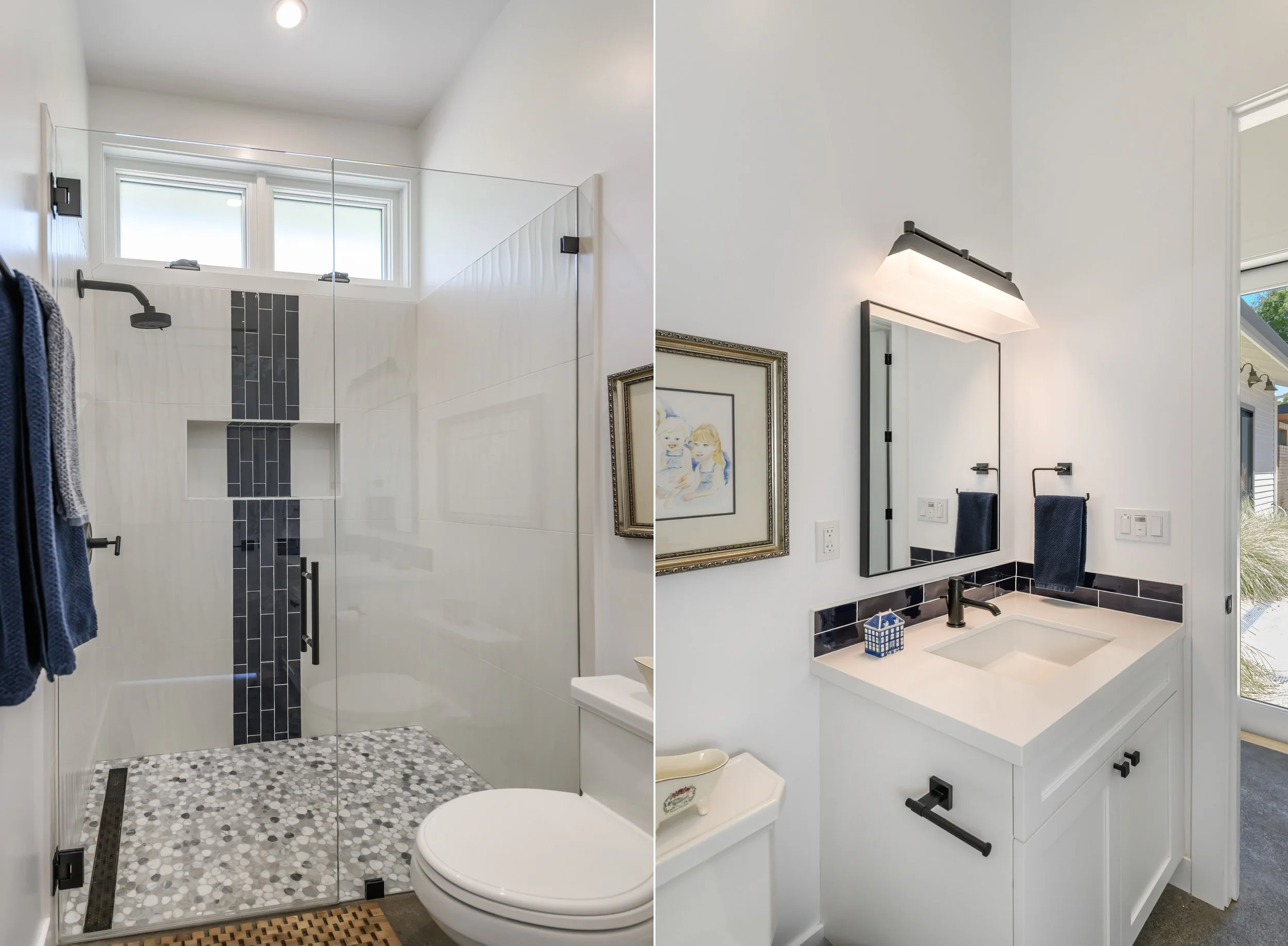 Bathroom with a separate shower on the left, featuring white tile walls with black vertical mosaic accents, pebble floor, and two small high windows; and a white vanity with a black faucet, mirror, framed picture, and dark blue towels on the right.