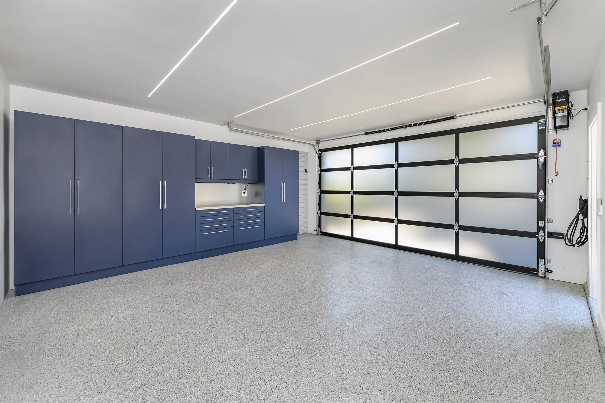 Empty garage with blue cabinets, concrete floor, and frosted glass garage door with black framing.