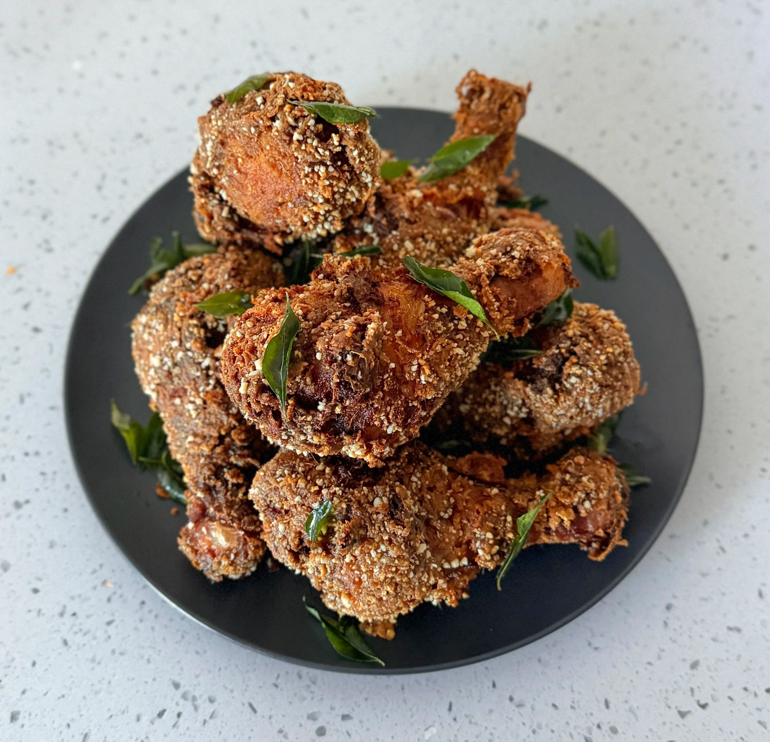 golden brown fried chicken topped with curry leaves on a modern simple minimal grey plate