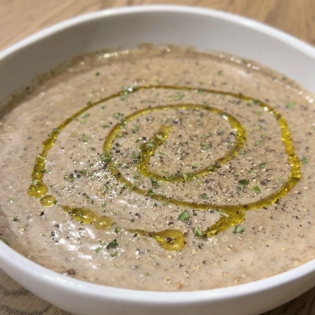 vegan cream of mushroom soup drizzled with olive oil, freshly cracked black pepper, dried parsley, served in a neutral toned, beige bowl