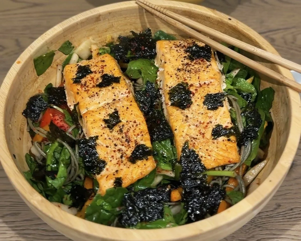 Cold soba noodles with salad greens, tomatoes, onions, kimchi, bell peppers, shredded seaweed and baked salmon. Served in a bamboo bowl and a pair of bamboo chopsticks.