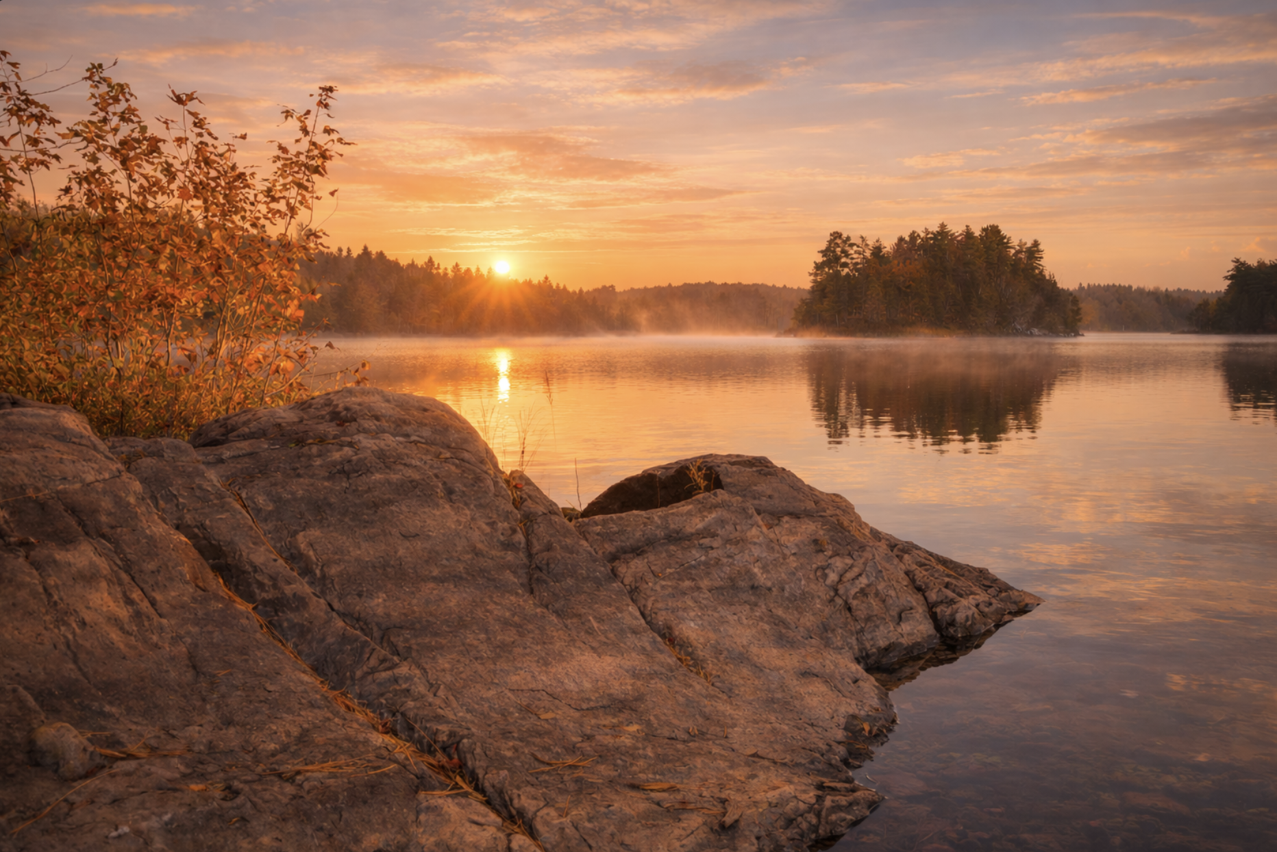 Warm sunrise over a peaceful Ontario lake with golden light reflecting across the water and rocky shoreline, representing hope, steadiness, and emotional healing through virtual therapy at Watkins Counselling & Wellness.