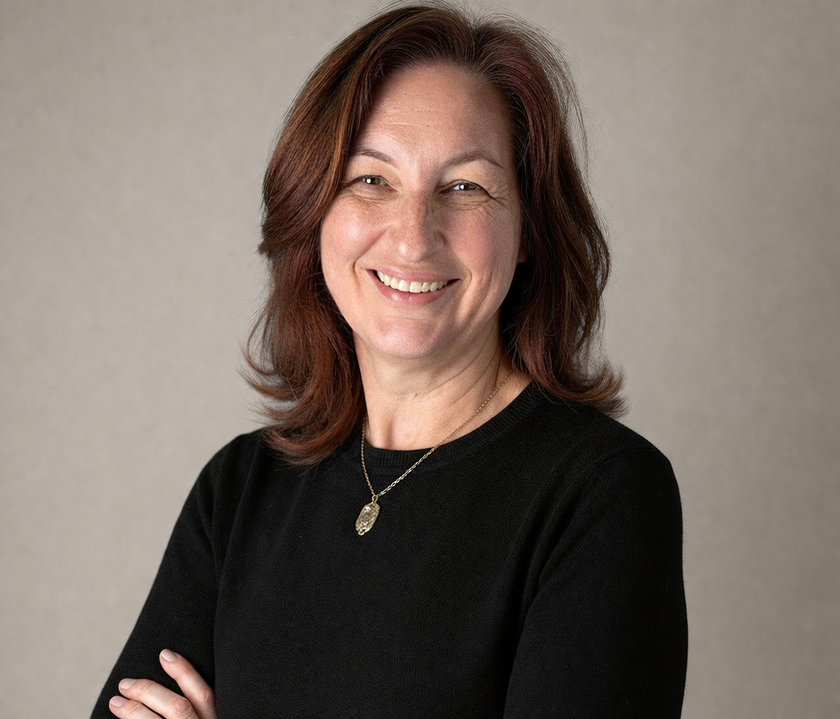 Nicola Wolters- Registered Psychotherapist (Qualifying) with reddish-brown hair, smiling and wearing a black top, standing against a neutral background.