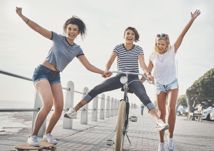 Three friends smiling and laughing together outdoors, enjoying each other’s company on a sunny day.