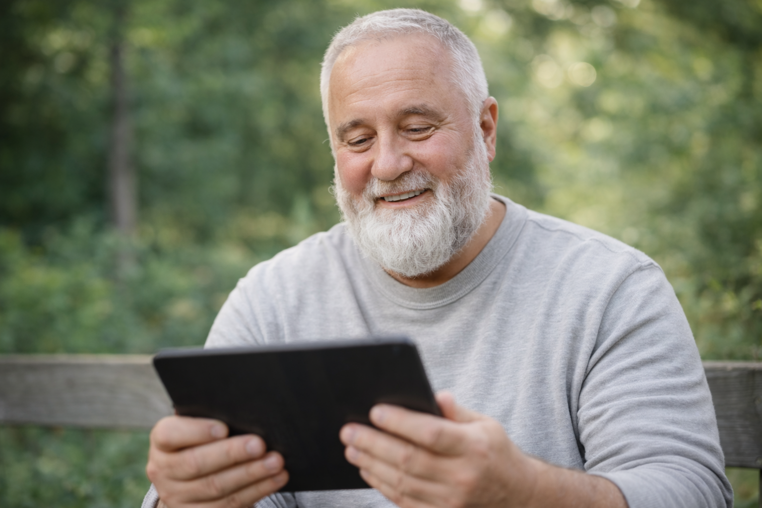 Older man smiling while using a tablet outdoors during virtual individual counselling in Ontario.