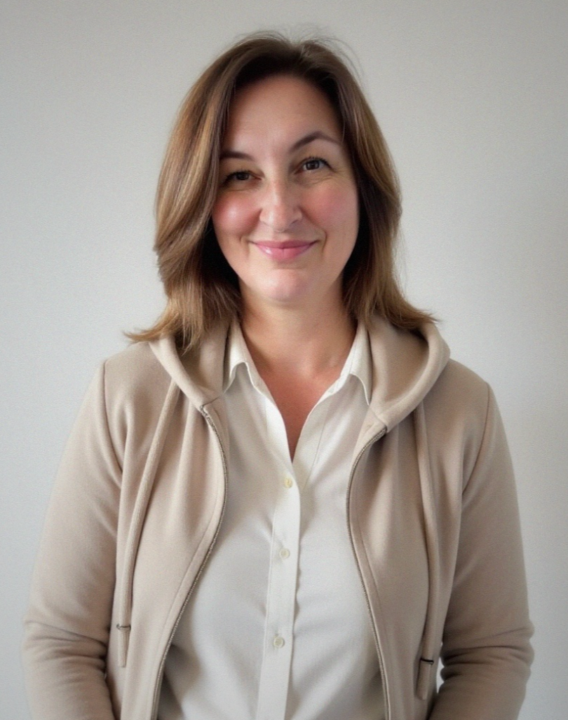 Photo of Nicola Wolters- Registered Psychotherapist (Qualifying). A woman with shoulder-length brown hair, wearing a beige hoodie over a white button-up shirt, smiling against a plain light-colored background.